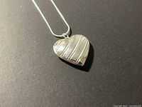 Heart locket pendant on chain, diagonal stripe design visible