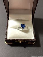 Front view of ring in box showing blue heart stone and accent stones