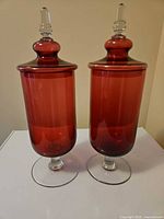 Front view of both cranberry glass jars with lids in place