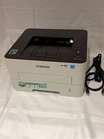 Front and top view of Samsung Xpress M2835DW printer with attached labels and cables