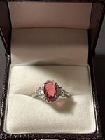 Ring in display box showing oval pink gemstone and clear accents
