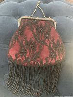 Front view showing red fabric, black lace overlay, bead fringe and chain strap