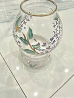 Globe shade atop base showing floral painting and gold rim