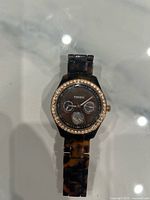 Front view of watch showing dial, crystal bezel, and tortoiseshell bracelet