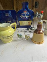 Group shot showing Crown Royal tins, Canadian Club dispenser, Dewar’s pitcher, Bell’s decanter, two loose shot glasses