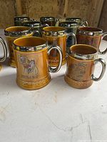 Group of amber glaze steins showing printed scenes and metallic accents