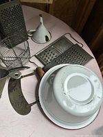 Group view of vintage graters, enamelware bowl and funnel, wire strainer, scoop and chopper