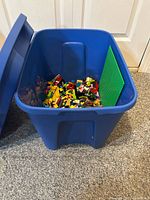 Blue bin with lid opened showing mixed LEGO pieces and green baseplate