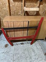 Red wooden buck saw leaning against cabinets