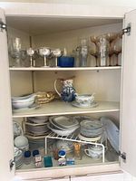 Cabinet view showing stacks of plates, bowls, teacups, pitcher, gravy boat, dessert cups, glassware