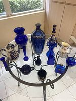 Full group on glass table showing majority of items including genie bottle, vases, teapots, pitcher