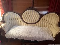 Front view of carved wood settee with cream velvet upholstery and crocheted cover on seat