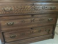Front view showing oak construction, four drawers, carved motifs, brass hardware