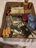 Overview of box showing mix of utensils, leather goods, mold, wooden pestle and cardboard box