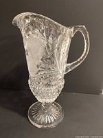 Full view of clear cut glass pitcher showing floral etch, handle, pedestal base