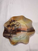 Ruffled round dish with handle showing painted landscape