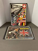 Both poster prints shown upright: Zurich & Berne Cycliste poster at back, Raleigh advertisement at front