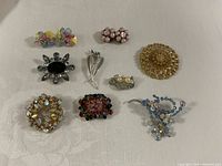 All seven brooches and two pairs of clip-on earrings displayed on white cloth