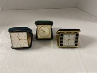 Front view of all three folding travel alarm clocks in cases