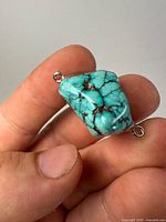 Front view of polished turquoise stone with silver-tone mounts and two loops