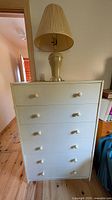Front view of white six-drawer dresser with beige ceramic table lamp on top