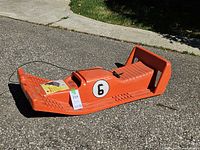 Side view of orange Sno-Jag Blazer sled showing number 6 decal, pull rope, instruction pamphlet