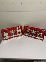 Two boxed sets of three silver-tone stocking holders displayed