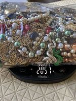 Bag of mixed costume jewelry on scale showing weight 2057 g