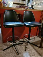 Both bar stools front view showing upholstery, bases, and chrome footrest rings