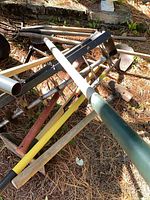 Overall view of assorted long-handled garden tools and aerator lying on ground