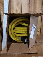 Coiled yellow cable inside open box showing plug