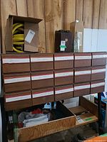Front view of wood cabinet showing four rows of five labeled drawers