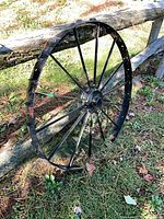 Front view of full cast iron wagon wheel leaning on wooden fence