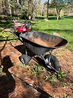 Full view of black 3-wheel wheelbarrow showing front pneumatic wheel, rear stabilizer wheels, steel tray and handles