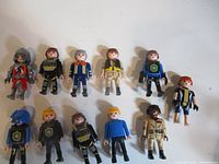 Group shot of all eleven Playmobil figures laid out on white surface showing fronts, uniforms and helmets