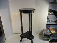 Full view of black wood plant stand showing round top, four legs, tripod base