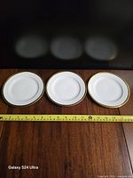 front view of three plates showing gold rim and tape measure indicating 6" diameter