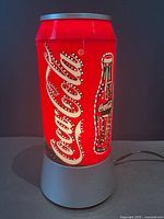 Front view of red Coca-Cola can lamp illuminated, cord visible