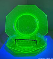 Five stacked octagonal uranium glass plates glowing under UV light