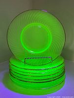 Stack of eight uranium glass plates glowing under UV light, showing swirl pattern and gold rims