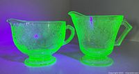 Two uranium glass creamers glowing under UV light