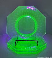 Four octagonal uranium glass dishes glowing green under UV light, stacked on stand