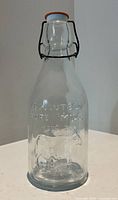 Front view of clear glass milk bottle with bail stopper, showing embossed cow graphic and text