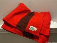 Folded red wool blanket with brown stripe displayed on ledge