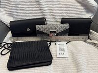 Front view of all three black purses with straps and grey Guess wallet, ruler for scale