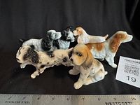 Front view of all six ceramic dog figurines with ruler for scale
