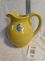 Front view of yellow ceramic jug showing sticker and handle