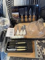 Grouped lot showing packaged knife set, mortar and pestle, cheese board, additional knife sets and wire tray