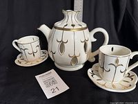 Ivory ceramic teapot with gold trim and two matching cups on saucers