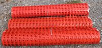 Three rolled orange plastic safety fences on gravel